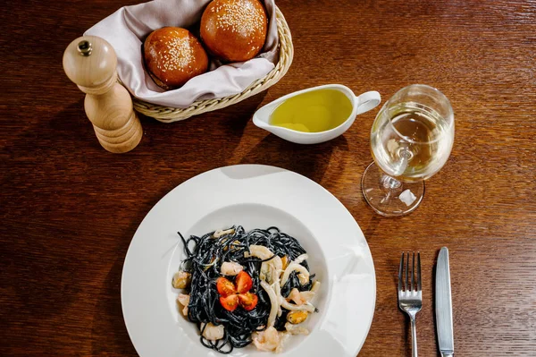 Fekete spagetti. Fűszeres fekete tenger gyümölcsei tészta tintahallal bazsalikommal a fa asztalon. — Stock Fotó