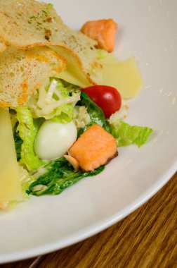 Beyaz tabakta somon salatası ve ahşap arka planda Sezar salatası. Somonlu Sezar salatası.