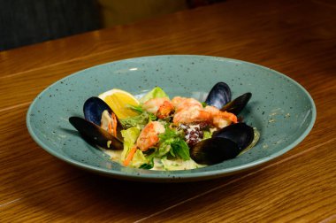 İstiridyeli salata, karides ve sebze mavi tabakta ahşap arka planda, üst manzara