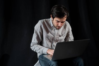 İyi niyetli iş adamı dizüstü bilgisayar kullanıyor. Tişörtlü mutlu adam karanlık bir arka planda dizüstü bilgisayarda çalışıyor. Genç adam dizüstü bilgisayarı üzerinde çalışıyor.