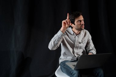 İyi niyetli iş adamı dizüstü bilgisayar kullanıyor. Tişörtlü mutlu adam karanlık bir arka planda dizüstü bilgisayarda çalışıyor. Genç adam dizüstü bilgisayarı üzerinde çalışıyor.