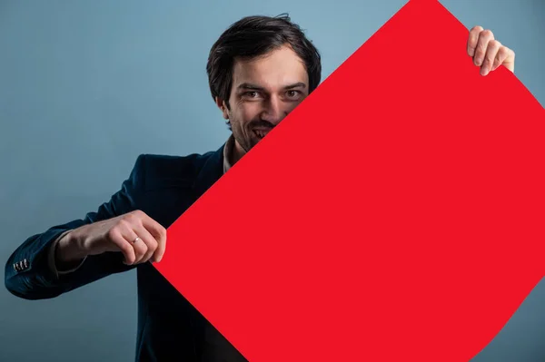 Happy man holding a red poster.Happy smiling young man showing blank signboard with empty copyspace area for slogan or advertising text message. Caucasian male model in advertisiment concept.