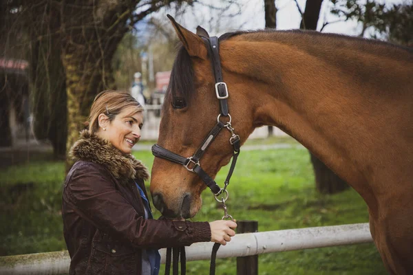 Wesoła Uśmiechnięta Kobieta Ubrana Brązową Kurtkę Patrząca Swojego Konia Ranczu — Zdjęcie stockowe