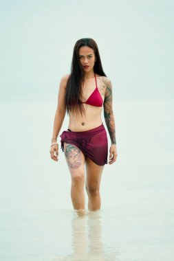 Arkadan yakalanan, dövmeli bir kadın sakince denize doğru yürüyor, uzun saçları akıyor ve ışık nazik dalgalardan yansıyor. Doğayla olan bu sessiz bağ, özgürlüğü, farkındalığı ve kişisel gücü yansıtıyor. Sağlıklı olmak için mükemmel.