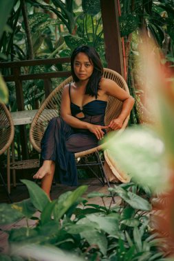 Lüks botanik ortamında yalınayak rahatlayan zarif genç bir kadın sakin bir güven, kadınlık ve huzurlu bir tatil yaşam tarzı iletiyor..