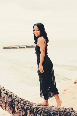 Kendine güveni tam bir kadın okyanusun kenarındaki bir palmiye gövdesinde yalınayak dengede duruyor. Özgürlüğünü, macerasını ve sıcak bir sahil seyahati havasını ifade ediyor..