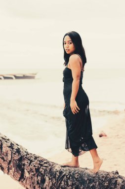 Kendine güveni tam bir kadın okyanusun kenarındaki bir palmiye gövdesinde yalınayak dengede duruyor. Özgürlüğünü, macerasını ve sıcak bir sahil seyahati havasını ifade ediyor..