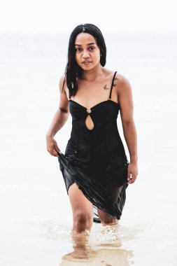 Sakin deniz suyundan çıkan kendine güvenen bir kadının tek renkli görüntüsü, minimalist bir kıyı ortamında güç, özgürlük ve duygusal yoğunluğu ifade ediyor..