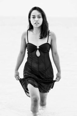 Sakin deniz suyundan çıkan kendine güvenen bir kadının tek renkli görüntüsü, minimalist bir kıyı ortamında güç, özgürlük ve duygusal yoğunluğu ifade ediyor..