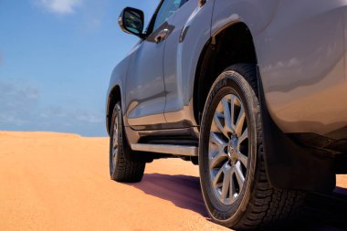 Araba, çölün ortasında parlak mavi bir gökyüzüne karşı duruyor.