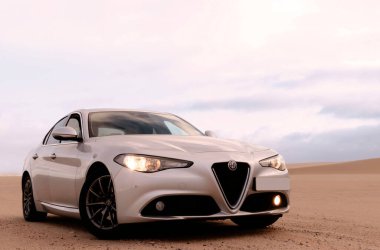 Alfa Romeo Giulia bulutlu gökyüzüne karşı altın kumda duruyor. 12.07.2021. Svakopmund. Namibya. Afrika