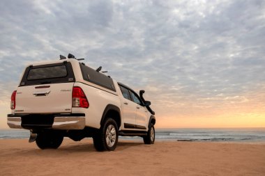 Toyota Hilux, Atlantik Okyanusu kıyısında parlak dramatik bir günbatımında duruyor. 19.07.2021. Namibya. Afrika