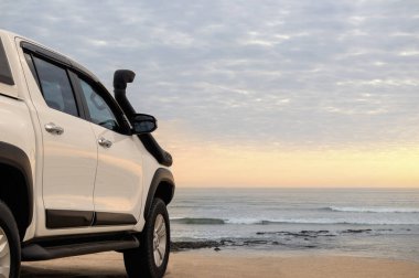 Beyaz off-road arabası Atlantik okyanusunun kıyısında duruyor. Parlak dramatik bir günbatımında.