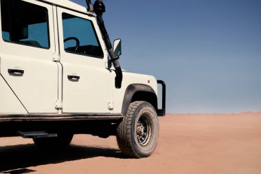 Güneşli bir günde Namib Çölü 'nün kırmızı kumlarında beyaz bir araba duruyor. 23.08.2021. Sossusvlei, Namibya