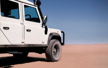 Güneşli bir günde Namib Çölü 'nün kırmızı kumlarında beyaz bir araba duruyor. 23.08.2021. Sossusvlei, Namibya