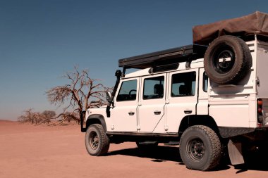 Güneşli bir günde Namib Çölü 'nün kırmızı kumlarında bir off-road arabası duruyor. Sossusvlei, Namibya. Afrika