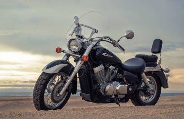 Canlı bir günbatımı gökyüzünün altında park etmiş bir motosiklet, özgürlük, macera ve bağımsızlığı çağrıştırıyor, ve açık yolların ruhunu yansıtıyor, kişisel keşifler, ve ufkun ötesine geçmek için sonsuz arzu..