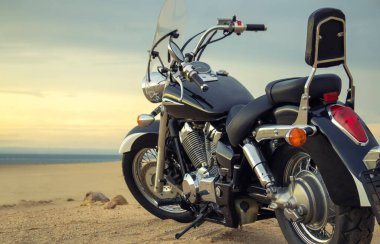 Canlı bir günbatımı gökyüzünün altında park etmiş bir motosiklet, özgürlük, macera ve bağımsızlığı çağrıştırıyor, ve açık yolların ruhunu yansıtıyor, kişisel keşifler, ve ufkun ötesine geçmek için sonsuz arzu..