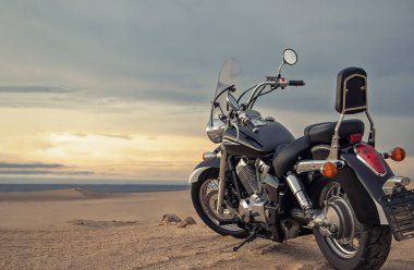 Canlı bir günbatımı gökyüzünün altında park etmiş bir motosiklet, özgürlük, macera ve bağımsızlığı çağrıştırıyor, ve açık yolların ruhunu yansıtıyor, kişisel keşifler, ve ufkun ötesine geçmek için sonsuz arzu..
