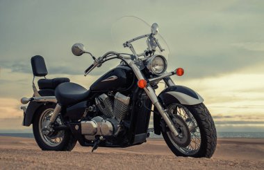 Bir motosiklet, gün batımında canlı bir gökyüzünün altında duruyor. Güçlü bir özgürlük, macera ve bağımsızlık hissi yakalıyor. Açık yolların, kişisel yolculukların ve yeni ufukların keşfinin heyecanını sembolize ediyor..