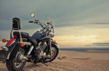 Bir motosiklet, gün batımında canlı bir gökyüzünün altında duruyor. Güçlü bir özgürlük, macera ve bağımsızlık hissi yakalıyor. Açık yolların, kişisel yolculukların ve yeni ufukların keşfinin heyecanını sembolize ediyor..