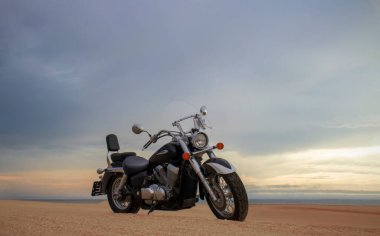 Canlı bir günbatımı gökyüzünün altında park etmiş bir motosiklet, özgürlük, macera ve bağımsızlığı çağrıştırıyor, ve açık yolların ruhunu yansıtıyor, kişisel keşifler, ve ufkun ötesine geçmek için sonsuz arzu..