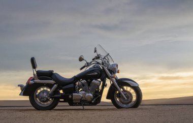 Canlı bir günbatımı gökyüzünün altında park etmiş bir motosiklet, özgürlük, macera ve bağımsızlığı çağrıştırıyor, ve açık yolların ruhunu yansıtıyor, kişisel keşifler, ve ufkun ötesine geçmek için sonsuz arzu..