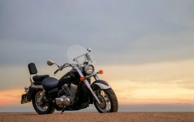 Canlı bir günbatımı gökyüzünün altında park etmiş bir motosiklet, özgürlük, macera ve bağımsızlığı çağrıştırıyor, ve açık yolların ruhunu yansıtıyor, kişisel keşifler, ve ufkun ötesine geçmek için sonsuz arzu..