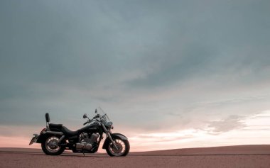 Canlı bir günbatımı gökyüzünün altında park etmiş bir motosiklet, özgürlük, macera ve bağımsızlığı çağrıştırıyor, ve açık yolların ruhunu yansıtıyor, kişisel keşifler, ve ufkun ötesine geçmek için sonsuz arzu..