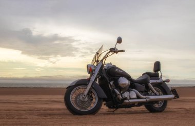 Canlı bir günbatımı gökyüzünün altında park etmiş bir motosiklet, özgürlük, macera ve bağımsızlığı çağrıştırıyor, ve açık yolların ruhunu yansıtıyor, kişisel keşifler, ve ufkun ötesine geçmek için sonsuz arzu..