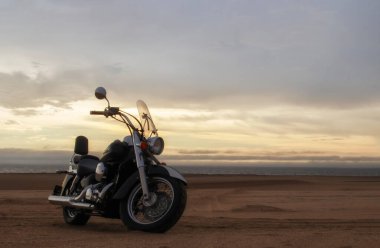 Canlı bir günbatımı gökyüzünün altında park etmiş bir motosiklet, özgürlük, macera ve bağımsızlığı çağrıştırıyor, ve açık yolların ruhunu yansıtıyor, kişisel keşifler, ve ufkun ötesine geçmek için sonsuz arzu..