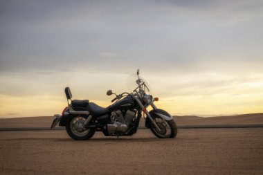 Canlı bir günbatımı gökyüzünün altında park etmiş bir motosiklet, özgürlük, macera ve bağımsızlığı çağrıştırıyor, ve açık yolların ruhunu yansıtıyor, kişisel keşifler, ve ufkun ötesine geçmek için sonsuz arzu..