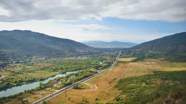 Scenic panoramic top view to road crossing a valley of Aragvi river, Tbilisi suburban towns and villages, rich farmland on blurred background of stunning Caucasus mountains,Georgia.