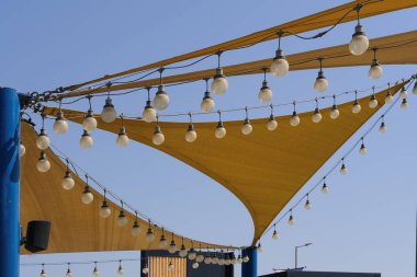 Kumaşın dinamik dokusu, mavi gökyüzü arka planında parti gecesi ışıklandırması için sıra sıra ampul lambalarıyla yelkenli yelkenli kumaştan yapılmış..