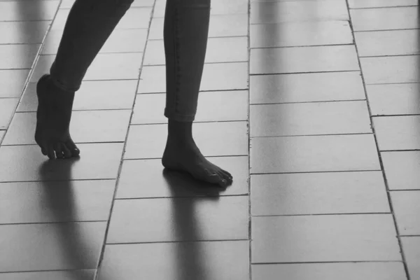 Абстрактные женские ноги лежат на плиточном полу, отбрасывая тени. Девушка ходит босиком по поверхности плитки, размытая в движении. силуэт шагающих женских ног. Лицензионные Стоковые Фото