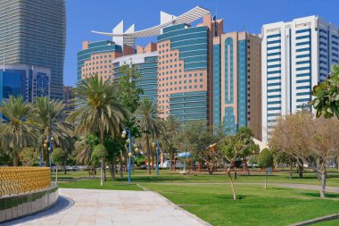 Cityscape with landscaped green public park with palm trees against modern residential buildings in Abu Dhabi, UAE