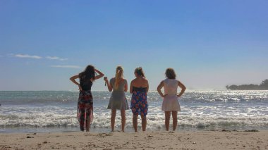 Sahilde dikilen ve uzak diyarlara bakan plaj elbiseli dört kız arkadaş grubuna. Genç kızlar plajda eğleniyor. SOFT FOCUS fotoğrafı. Mauritius, Afrika, Temmuz 2014