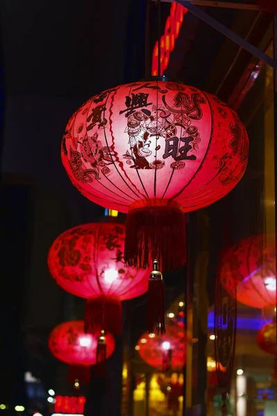 Papel tradicional Los faroles chinos rojos brillan en fila en la difusa calle nocturna. Celebración de Año Nuevo en Asia. Enfoque en primer plano. Imágenes de stock libres de derechos