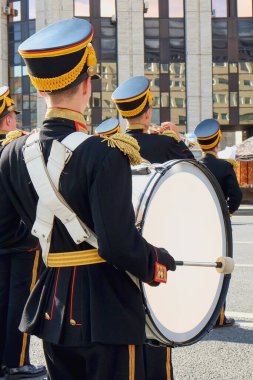 Şehir festivalinde siyah geçit töreni üniforması giymiş, sarı-kırmızı semboller ve altın püsküllü apoletler giyen, bulanık askeri orkestrayla birlikte beyaz bas davul çalan bir müzisyen. Moskova, Rusya, Sep 2019