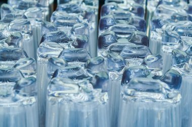 Sırayla dizilmiş saydam cam bardakların yakın plan görüntüsü. Cam tabanlar üzerindeki karmaşık ışık yansımaları modern, soyut bir doku yaratır, tasarım arka planlarında, restoran temalarında veya bar kavramlarında kullanılmak için idealdir..