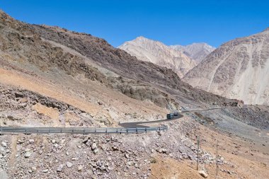 Ladakh, Kuzey Hindistan 'da dönen dağ yolunda giden iki araç. Kayalık çöl arazisi, dik yamaçlar ve açık mavi gökyüzü ile dramatik Himalaya manzarası. Himalayalar 'da seyahat.