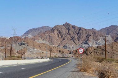 Kuzey Emirlikleri, Birleşik Arap Emirlikleri 'nde kayalık bir çöl arazisinde kıvrılan manzaralı dağ yolu. Uzak bir kurak bölgede seyahat, yolculuk, macera, özgürlük ve bağlantı kavramı.