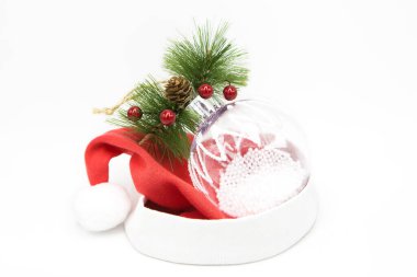 Şeffaf cam Noel ağacı oyuncağı beyaz arka planda izole edilmiş Noel Baba şapkasının içinde yatıyor. Noel ve Yeni Yıl şenlik geçmişi