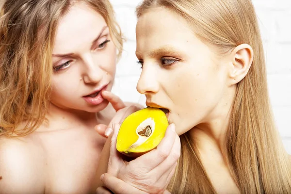 2人の若い美しい女性が抱き合って 白い背景に隔離されたジューシーなマンゴーフルーツをお互いに食べます 美とファッション — ストック写真