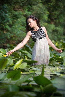 Güzel elbiseli genç bir kadın su zambaklarıyla gölün suyunda duruyor..