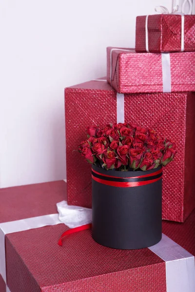 Beautiful bouquet of red roses in gift wrapping with silk ribbon and gift boxes. Holiday background.