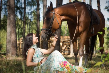 Ormandaki çimlerin üzerinde oturan ve nazikçe atına sarılan mutlu genç kız. Atı olan yürüyen bir kadın.