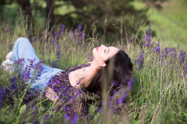 Genç ve rahat kız, çayırda güneşli bir günde kır çiçeklerinin ve çimenlerin arasında dinlenmenin keyfini çıkarıyor..