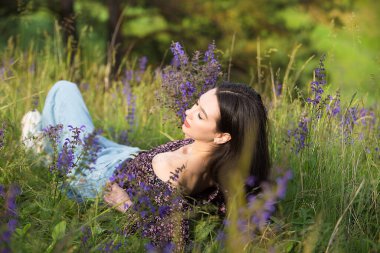 Genç ve rahat kız, çayırda güneşli bir günde kır çiçeklerinin ve çimenlerin arasında dinlenmenin keyfini çıkarıyor..