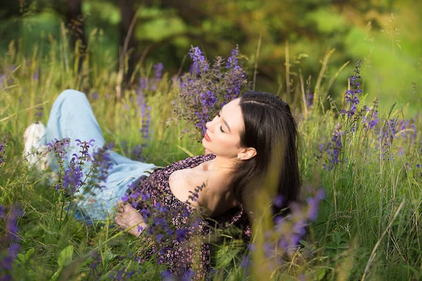 若いですリラックスした女の子楽しんで休息の間に横たわっている野生の花や草の間で晴れた日に牧草地で — ストック写真